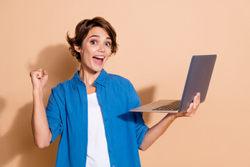 Photo of young successful lady in blue shirt raised fist up when buying goods auction using laptop...