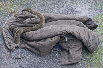 one crumpled green winter jacket lies on the gray asphalt in the street
