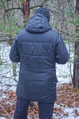 one man stands with his back in a winter jacket with a  hood and a black hat stands among white...