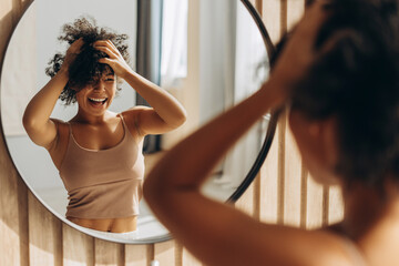 Happy woman styling her afro hair in front of mirror at home