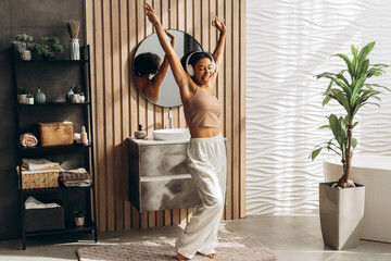 Happy woman listening music with headphones and dancing in modern bathroom