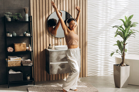 Happy woman listening music with headphones and dancing in modern bathroom - Powered by Adobe