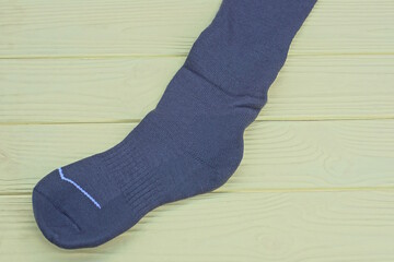 one gray long fabric sock lies on a yellow wooden table