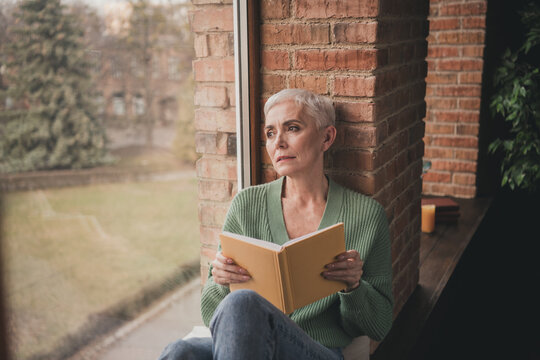 Elderly woman enjoys a peaceful reading moment by the window in a cozy living space - Powered by Adobe