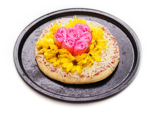 Pink roses and white chamomile flowers on top of a pizza and on dark metal cooking tray on white background. Abstract conceptual art.