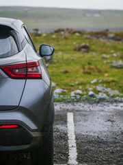 Grey car parked by a green field with many rock. Travel and explore nature concept. Rent a vehicle to tourist purpose. Sightseeing and hiking theme.