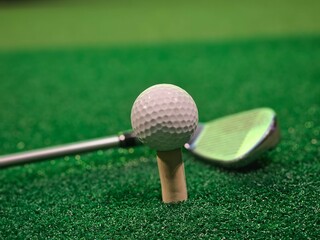 Golf ball on tee with club ready on green turf for an upcoming swing during