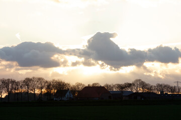 Rural Dutch landscape at sunset.  Silhouetted farm buildings and trees against a dramatic cloudy sky.