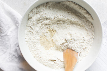 Overhead view of challah dough being mixed in a white bowl, top view of homemade challah dough being mixed on white granite countertop, process of making challah