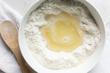 Overhead view of challah dough being mixed in a white bowl, top view of homemade challah dough being mixed on white granite countertop, process of making challah