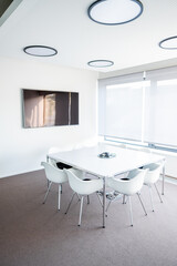 Modern Conference Room Featuring White Furniture, Video Conference Phone, and Large Screen Display
