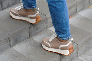 Stylish platform sneakers with white laces and brown soles stepping up brick stairs, modern...