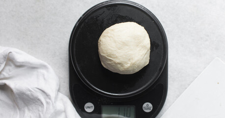 Overhead view of challah dough on a black kitchen scale, top view of homemade challah bread dough being weighed on a scale, process of making challah