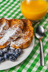 French toast on a white plate with blueberries and orange juice for breakfast