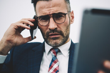 Half length portrait of confident middle aged entrepreneur looking at camera while calling on smartphone device.Serious executive manager 50 years old with touch pad in hand talking on mobile phone