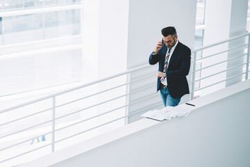 Top view of busy mature businessman talking on smartphone while looking at watch to checking time hurrying on meeting in office.Middle aged entrepreneur in formal wear calling on cellular device