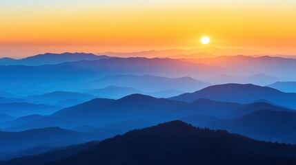 Fototapeta premium A stunning sunset over layered mountains, showcasing hues of orange and blue, creating a serene and tranquil landscape.