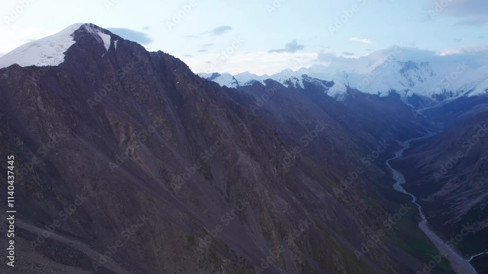 Wall mural View of the gorge with snow peaks in the distance. The drone is flying smoothly. A river runs through the gorge. High mountains with the majestic peak of Khan Tengri. A marble wall made of ice. Cloudy