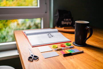 Creative Workspace with Craft Supplies and Open Book Resting on a Wooden Desk by a Window View