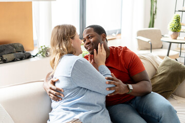 Relaxed middle aged multiethnic couple in casual clothes sitting together on sofa at home