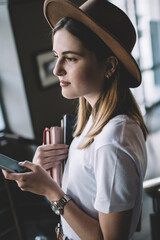 Serious caucasian woman 20s in stylish wear holding mobile phone dialling number indoors, pensive...