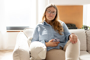 Obraz premium Portrait of middle aged woman in glasses with phone, sitting on the couch at home