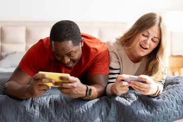 Portrait of happy multiethnic couple chatting online using smartphones in bedroom