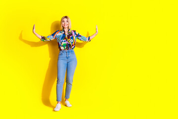 Full size photo of pretty young girl push side walls empty space wear trendy colorful outfit isolated on yellow color background