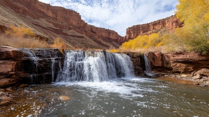 Obraz premium A serene waterfall cascading into a calm river, surrounded by autumn foliage and rocky cliffs.