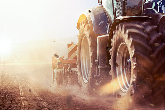 traktor auf dem Feld zieht Pflug oder Grubber, um den Boden aufzulockern und f&uuml;r die Aussaat vorzubereiten bei strahlendem Sonnenschein