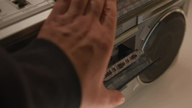 Close-Up Shows A Hand Carefully Placing A Cassette Tape Into A Vintage Music Player And Activating It. The Player Sits On A Table In A Light-Filled Room, Creating Nostalgic Vibes.