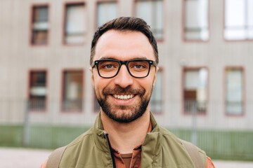 Portrait of happy, smiling bearded man wearing eyeglasses, looking at camera closeup on the street