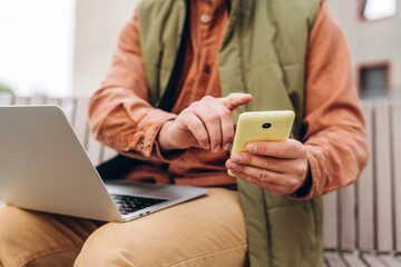 Portrait of man, freelancer wearing casual clothes, holding mobile phone, using laptop, text message
