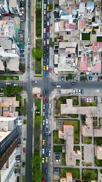 Tr&aacute;fico ligero de autom&oacute;viles y peatones transitando por la acera en un cruce de una avenida repleta de &aacute;rboles y rodeada de edificios, visto desde las alturas con un dron