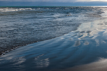 Lake Michigan waves wash onshore at Harrington Beach State Park, Belgium, Wisconsin in mid-November under dark clouds that allow only small sections of sunlight to sneek through