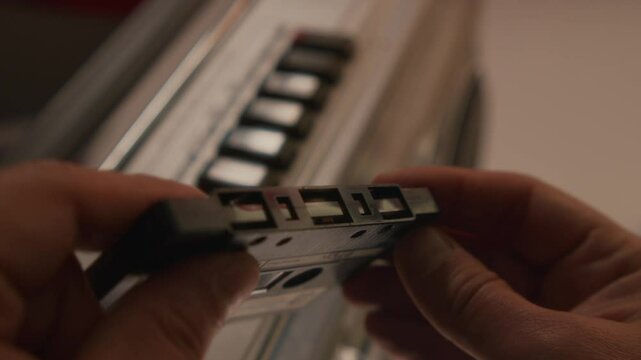 A Close-Up View Shows Hands Carefully Holding A Retro Cassette Tape. The Background Features A Classic 1985 Boombox, Evoking The Nostalgic Atmosphere Of Analog Music.