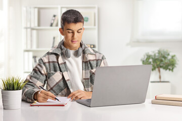 Male student with headphones writing and researching on a laptop computer