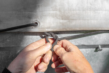 A man ties a tie-down cord on a car trailer tarpaulin. Cargo transportation