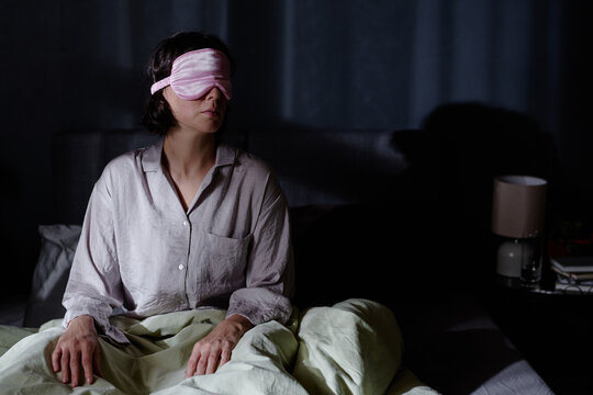 Woman with sleep mask rising from bed during late night at home