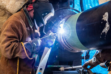 Schweißer bei der Arbeit an Rohrverbindung auf Baustelle
