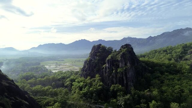 aerial view of ancient limestone rocky mountains, cliffs, and green trees with morning mist surrounded by rice fields. towering rocky hill of Sepikul mountain in Indonesia. 