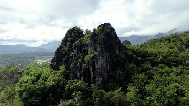 aerial view of ancient limestone rocky mountains, cliffs, and green trees with morning mist surrounded by rice fields. towering rocky hill of Sepikul mountain in Indonesia. 