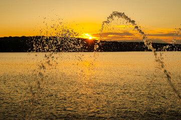 beautiful streams of water from fountains on the lake, reflection of sunset light in drops,...