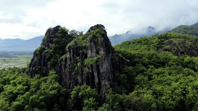aerial view of ancient limestone rocky mountains, cliffs, and green trees with morning mist surrounded by rice fields. towering rocky hill of Sepikul mountain in Indonesia. 