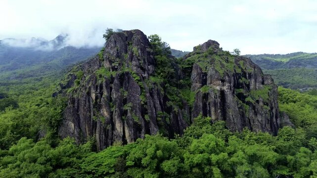 aerial view of ancient limestone rocky mountains, cliffs, and green trees with morning mist surrounded by rice fields. towering rocky hill of Sepikul mountain in Indonesia. 