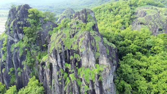 aerial view of ancient limestone rocky mountains, cliffs, and green trees with morning mist surrounded by rice fields. towering rocky hill of Sepikul mountain in Indonesia. 