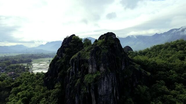 aerial view of ancient limestone rocky mountains, cliffs, and green trees with morning mist surrounded by rice fields. towering rocky hill of Sepikul mountain in Indonesia. 
