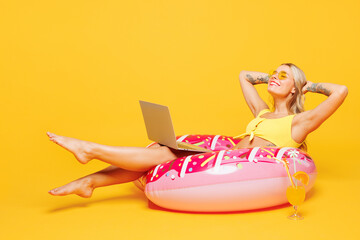Full body young IT woman wears bikini swimsuit rest near hotel pool lies on rubber ring work us laptop pc computer close eyes isolated on plain yellow background. Summer vacation sea sun tan concept.