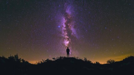 Person standing on hilltop gazing at stars and Milky Way galaxy in night sky. Silhouette of man against dark starry sky with purple orange hues.