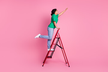 Full length photo of lovely young lady climbing ladder dressed stylish green garment isolated on pink color background © deagreez